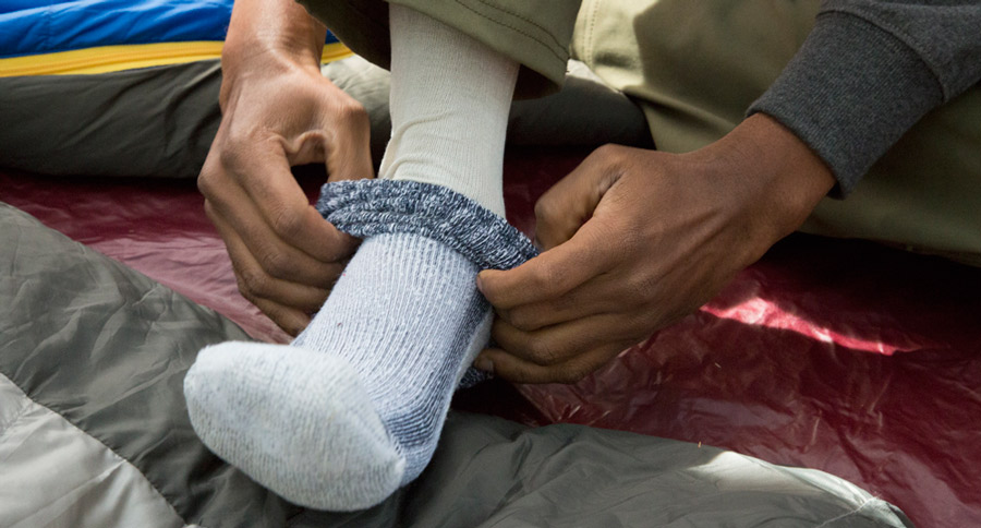 a hiker putting a hiker sock over their liner sock to prevent blisters