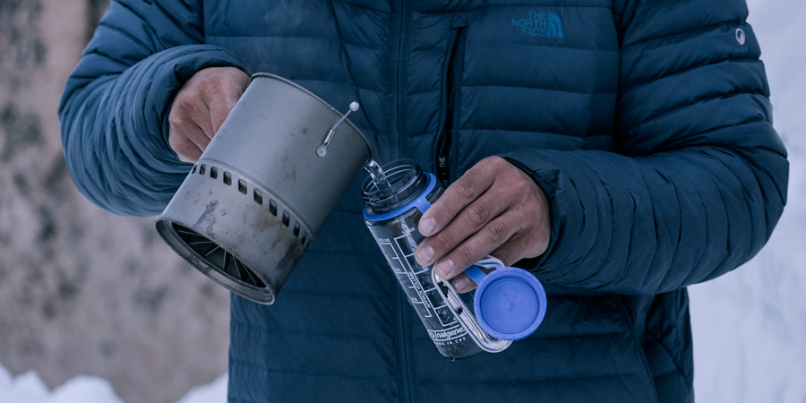 a hiker pouring warm water into a water bottle